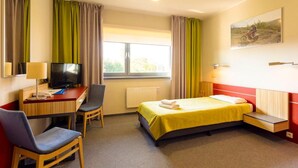 Habitación de hotel con cama, escritorio con televisor, una silla y ventana con cortinas.