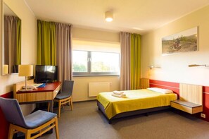 Habitación de hotel con cama, escritorio con televisor, una silla y ventana con cortinas.