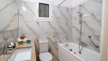 A bathroom with a marble wall, a bathtub, a toilet, and a sink.