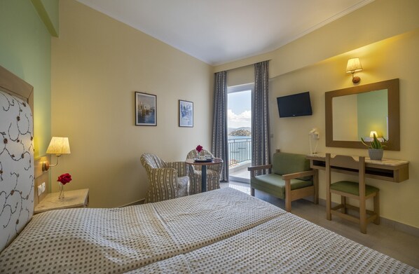 Habitación de hotel con cama, escritorio, silla, televisor y balcón con vistas.
