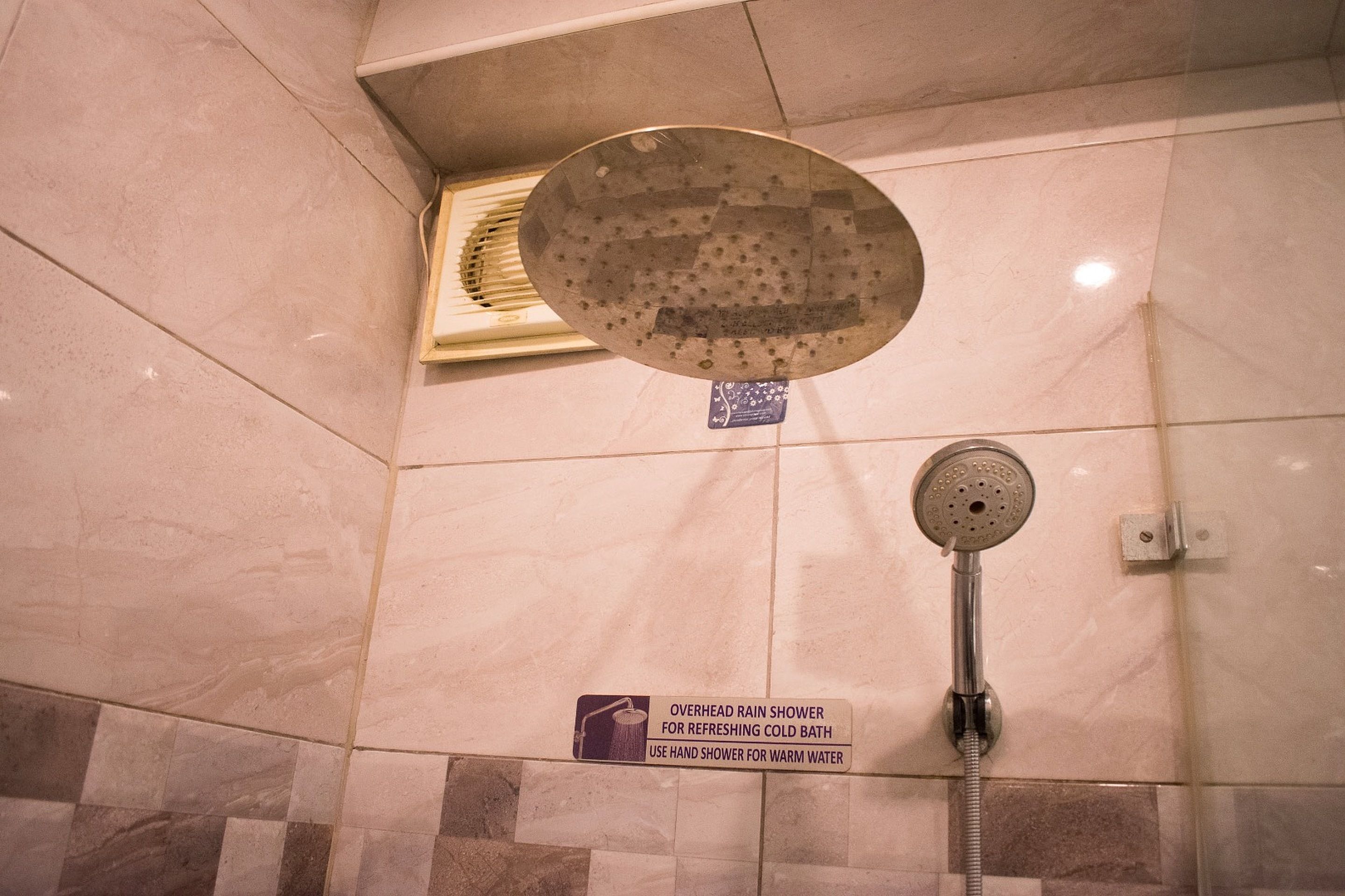 Un espace douche équipé d’une pomme de douche à pluie et d’un pommeau de douche à main, d’un panneau indiquant les instructions d’utilisation et d’un sol carrelé.