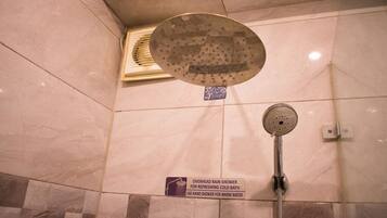 Un espace douche équipé d’une pomme de douche à pluie et d’un pommeau de douche à main, d’un panneau indiquant les instructions d’utilisation et d’un sol carrelé.