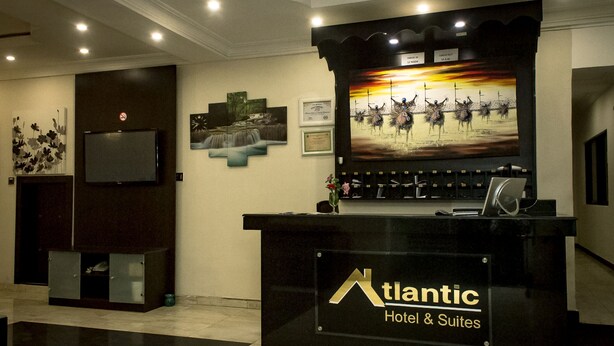 A reception desk with a sign for Atlantic Hotel & Suites, a television mounted on the wall, and framed artwork on the walls. - Atlantic Hotel And Suites (Lagos)