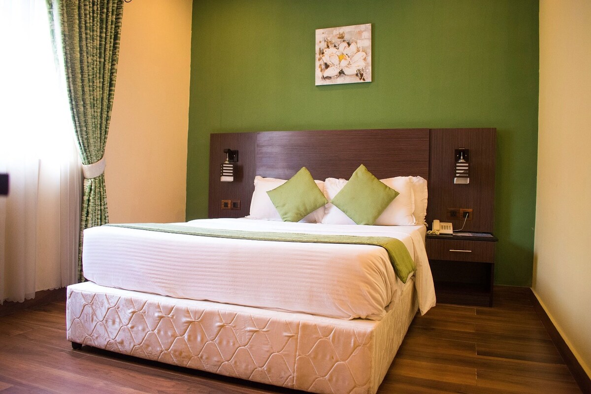 A neatly made bed with a quilted mattress and pillows, a bedside table with a lamp, and a wall-mounted artwork.
