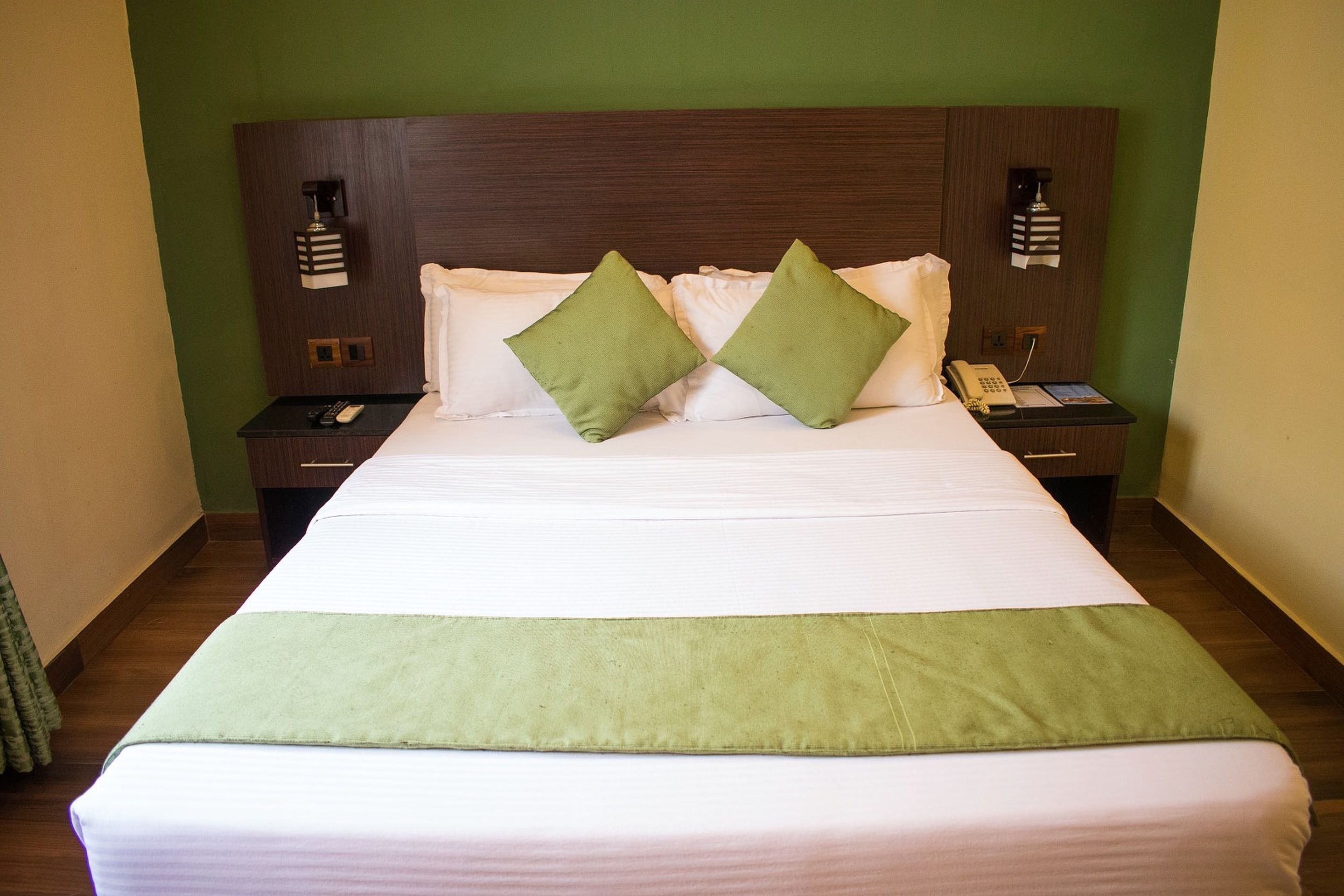 Una cama bien hecha con un plaid verde, dos almohadas verdes y un cabecero de madera.