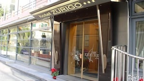 Entrada de un hotel con amplias puertas de vidrio y un letrero que dice "hotel ZURIGO".