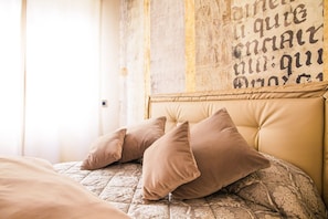 A bed with a patterned quilt and two pillows, a wall with a distressed design, and a door with a light switch. - Hotel Zurigo (Varazze)