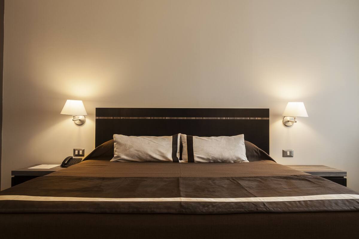 A neatly made bed with a dark headboard, two bedside lamps, and a telephone on the nightstand.