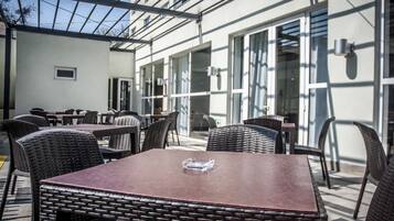 Un espacio de patio al aire libre con mobiliario de mimbre y una mesa con superficie de vidrio.