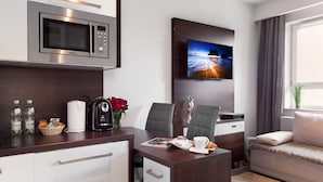 A modern hotel room with a kitchenette, a flat-screen TV, a sofa, and a desk with office supplies. - ActivPark Apartments (Katowice)