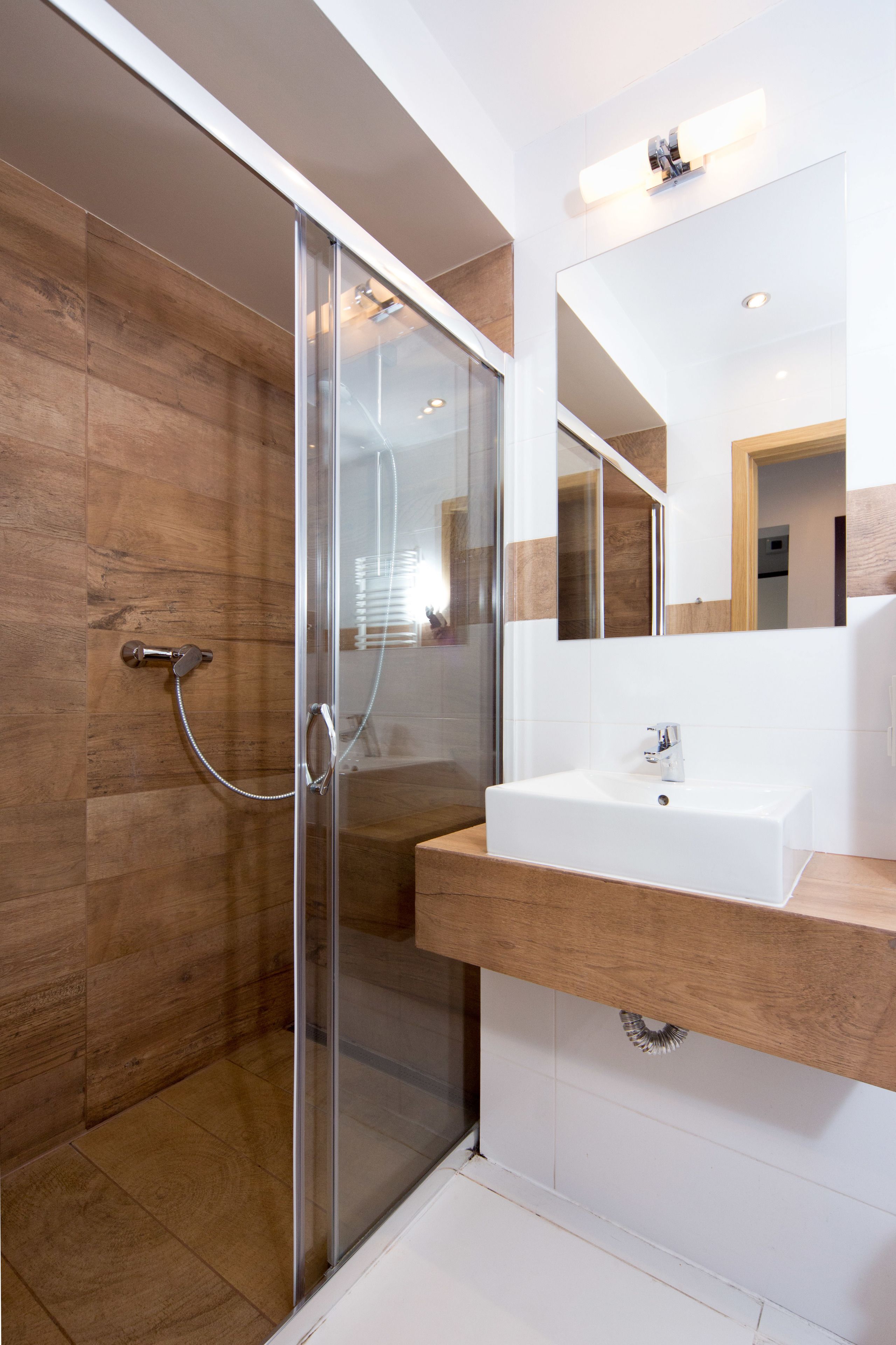 Une salle de bain moderne avec une douche à l’italienne en verre, un lavabo blanc et un meuble-lavabo en bois.