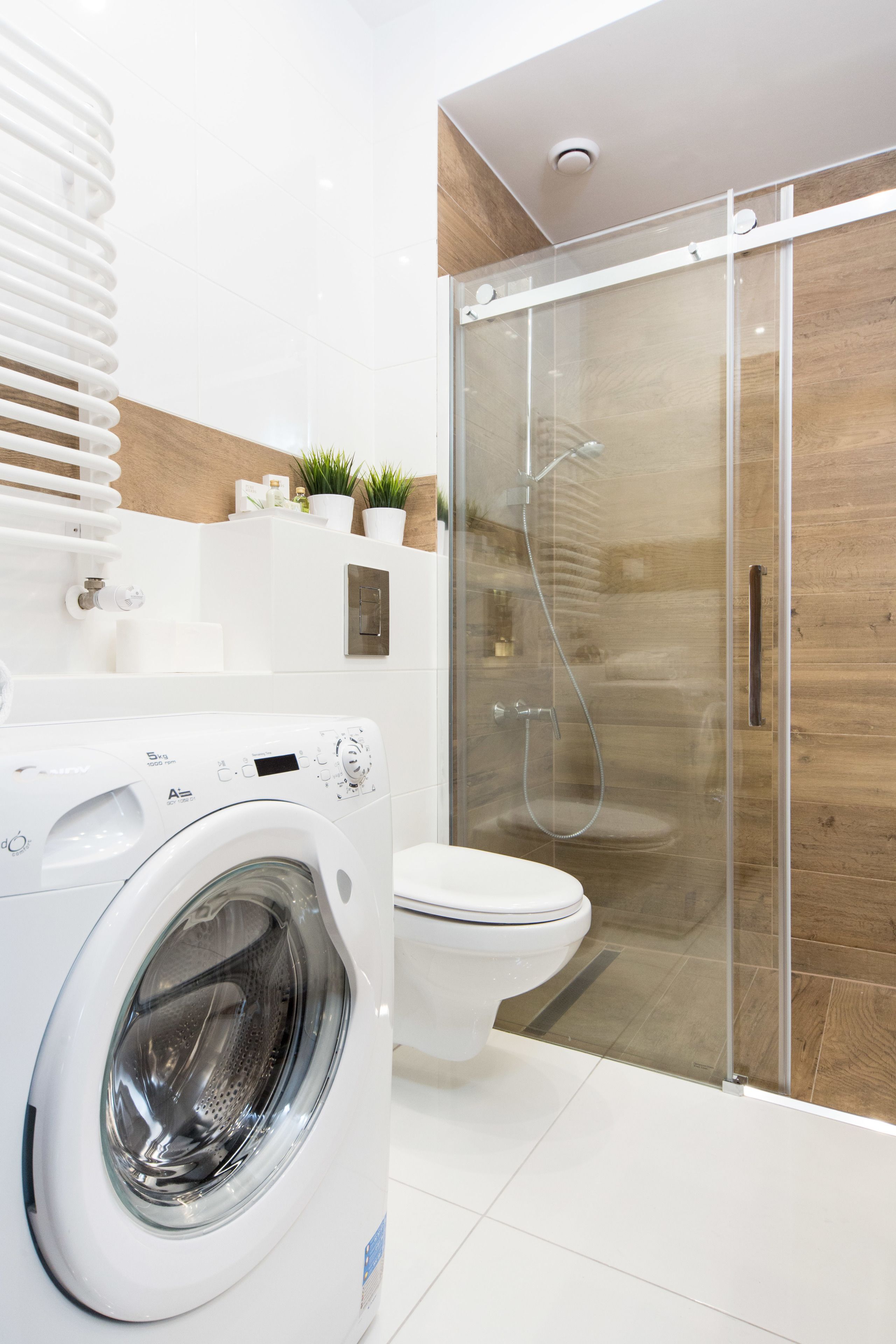 Et moderne badeværelse med en glasafskærmet brusekabine, en hvid vaskemaskine og et toilet.