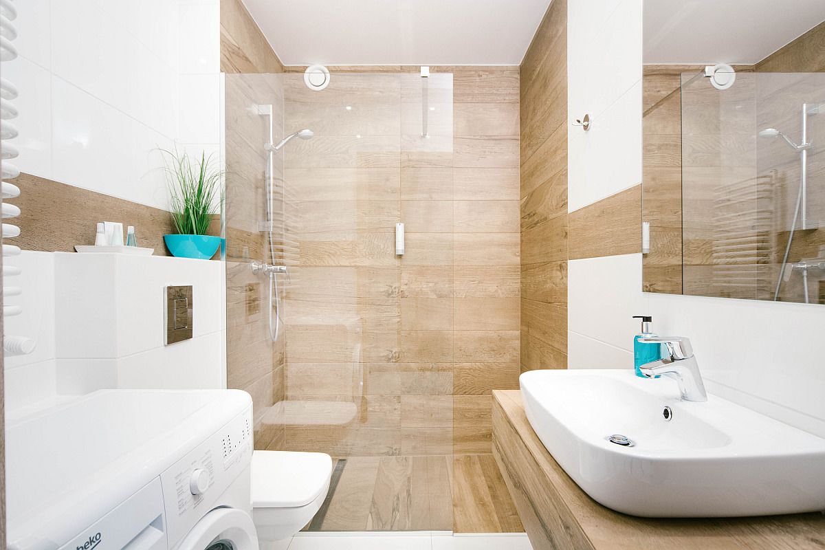 Un baño moderno con ducha envuelta en vidrio, un lavabo blanco y una lavadora.