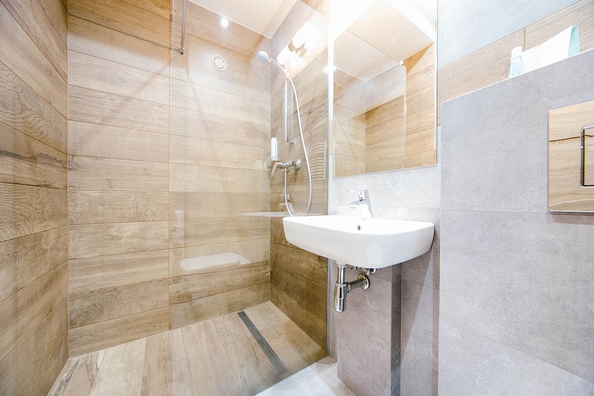 A modern bathroom with a wooden shower enclosure, a white sink, and a mirror.