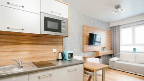A modern kitchen with a microwave, kettle, and coffee maker, a wooden dining table, and a built-in TV above a wooden cabinet. - ActivPark Apartments (Katowice)