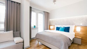 A modern hotel room with a large bed, a sofa, a nightstand, and a window with curtains. - ActivPark Apartments (Katowice)