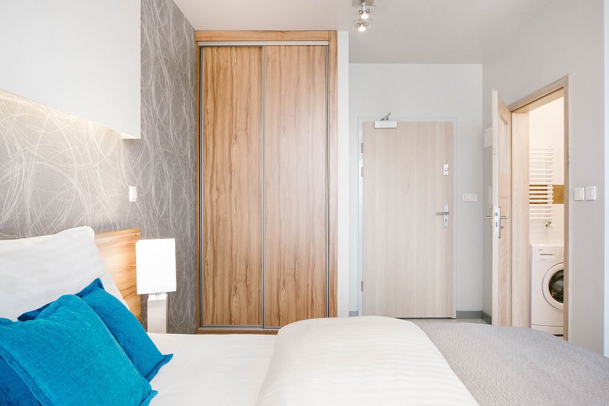Una habitación de hotel moderna con una cama grande, un armario de madera, una lavadora y un baño visible a través de una puerta abierta.