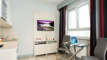 A modern kitchen with a built-in oven, a sink, and a countertop. There is a dining area with a glass table and two chairs. A painting is on the wall above the dining table.