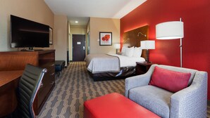 A hotel room with a bed, a desk, a TV, a sofa, and a red ottoman. - Best Western Plus Fairview Inn & Suites (Fairview)