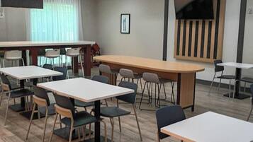 A modern indoor space with multiple tables and chairs, a large flat-screen TV mounted on the wall, and a wooden floor.