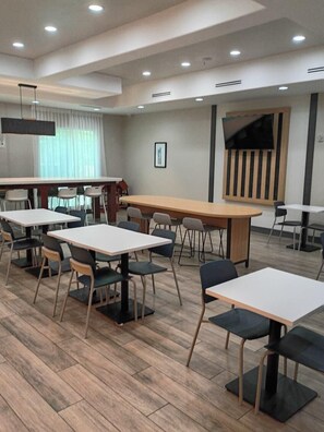 A modern indoor space with multiple tables and chairs, a large flat-screen TV mounted on the wall, and a wooden floor. - City Express by Marriott Spring (Spring)