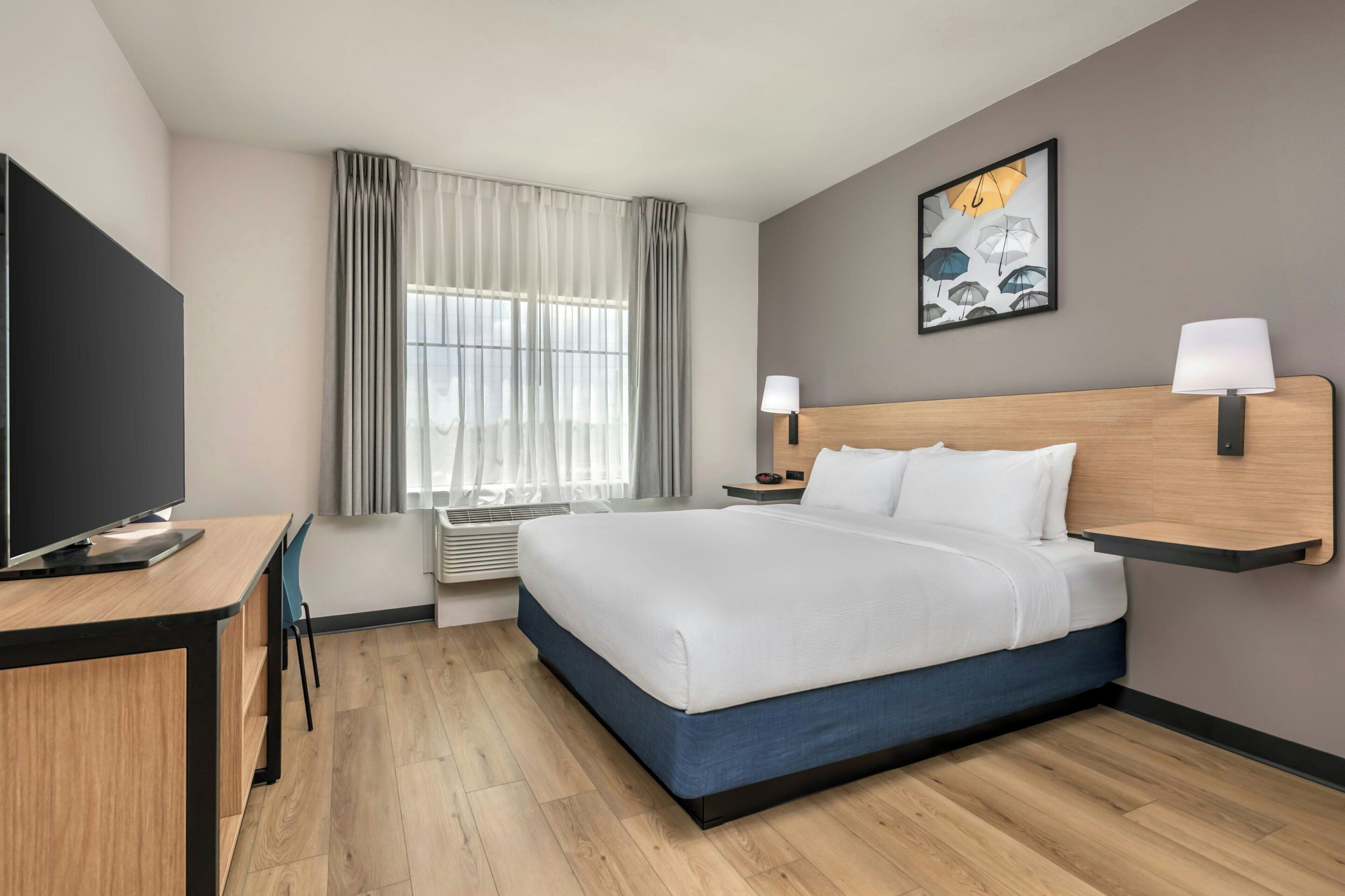 A hotel room with a bed, desk, chair, and a window with curtains.