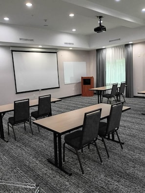 A conference room with a projector screen, tables, chairs, and a podium.
