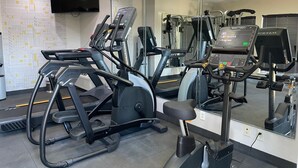 Une salle de sport équipée de tapis de course, de vélos elliptiques et d’un mur recouvert de miroirs.