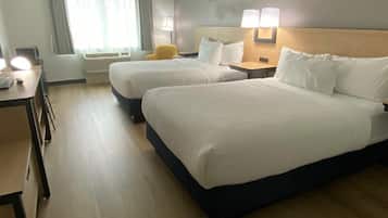 A hotel room with two beds, a desk, a chair, and a window with curtains.