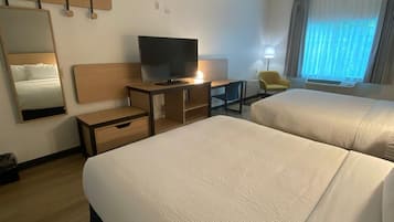 A hotel room with two beds, a desk with a TV, a chair, a mirror, and a window with curtains.