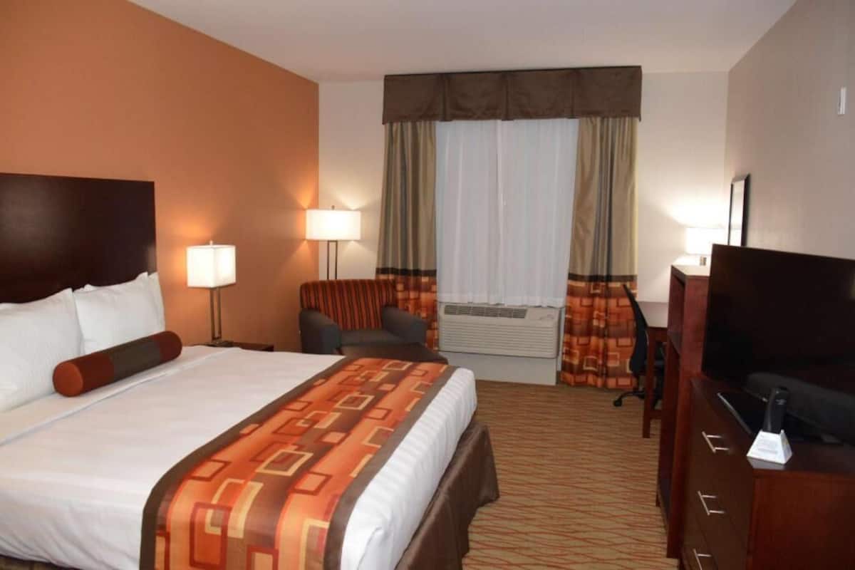 Una habitación de hotel con cama, dos lámparas de noche, televisor, escritorio y silla.