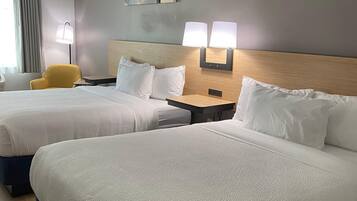 Habitación de hotel con dos camas, cabecero de madera, mesita de noche con lámparas, una silla amarilla y una obra de arte en la pared.