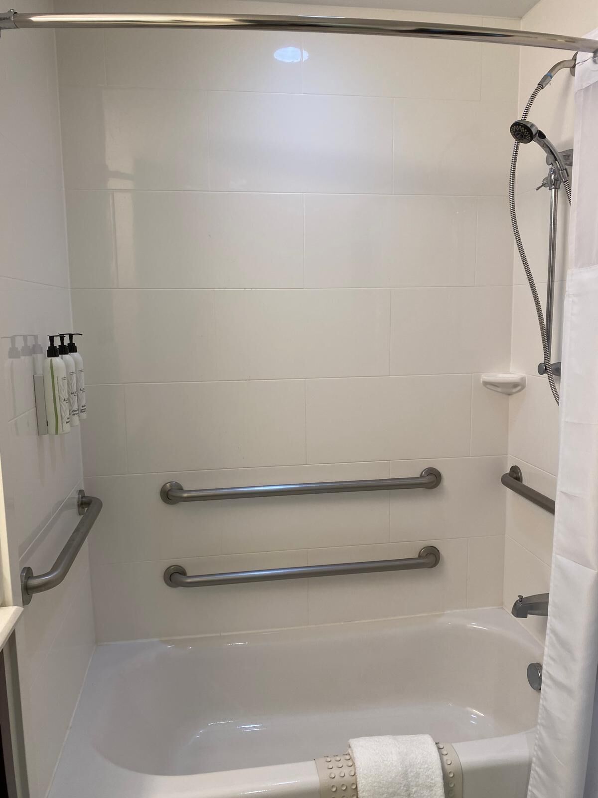 A shower area with a bathtub, grab bars, and a showerhead.