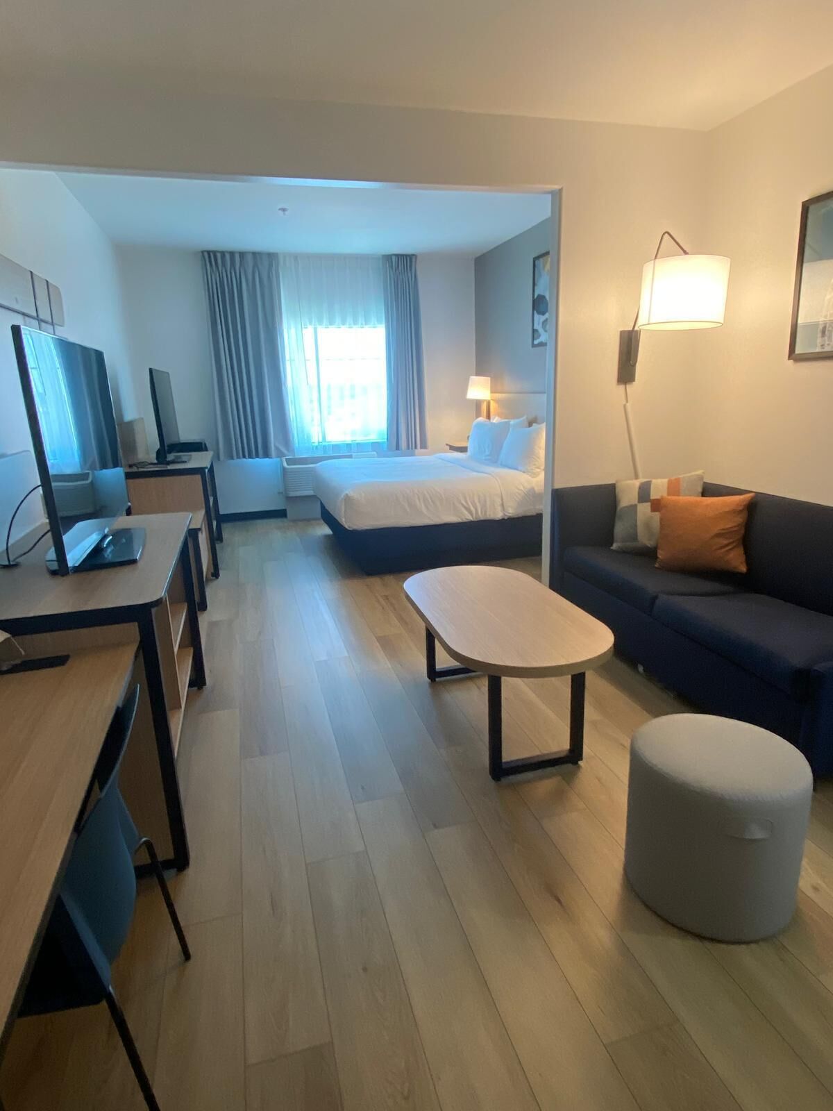 Habitación de hotel con cama, escritorio con computadora, sofá, una mesita y una lámpara.