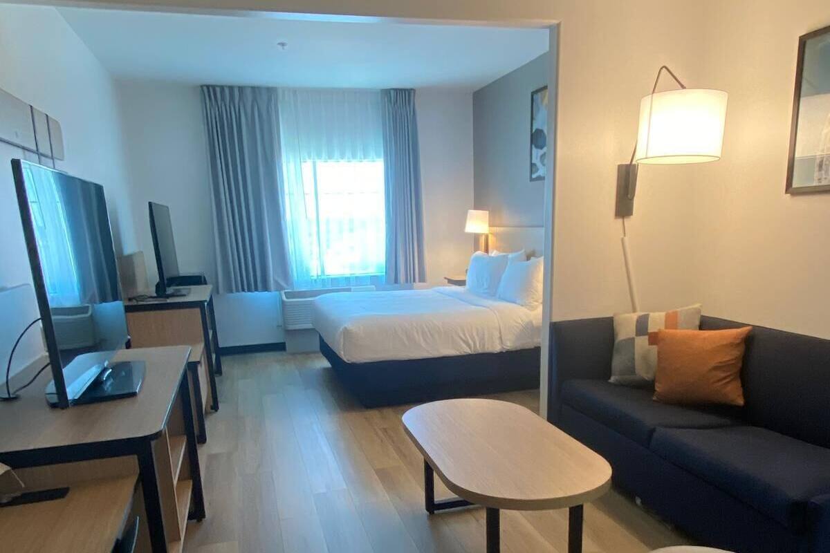 A hotel room with a bed, a desk with a computer, a sofa, a small table, and a lamp.