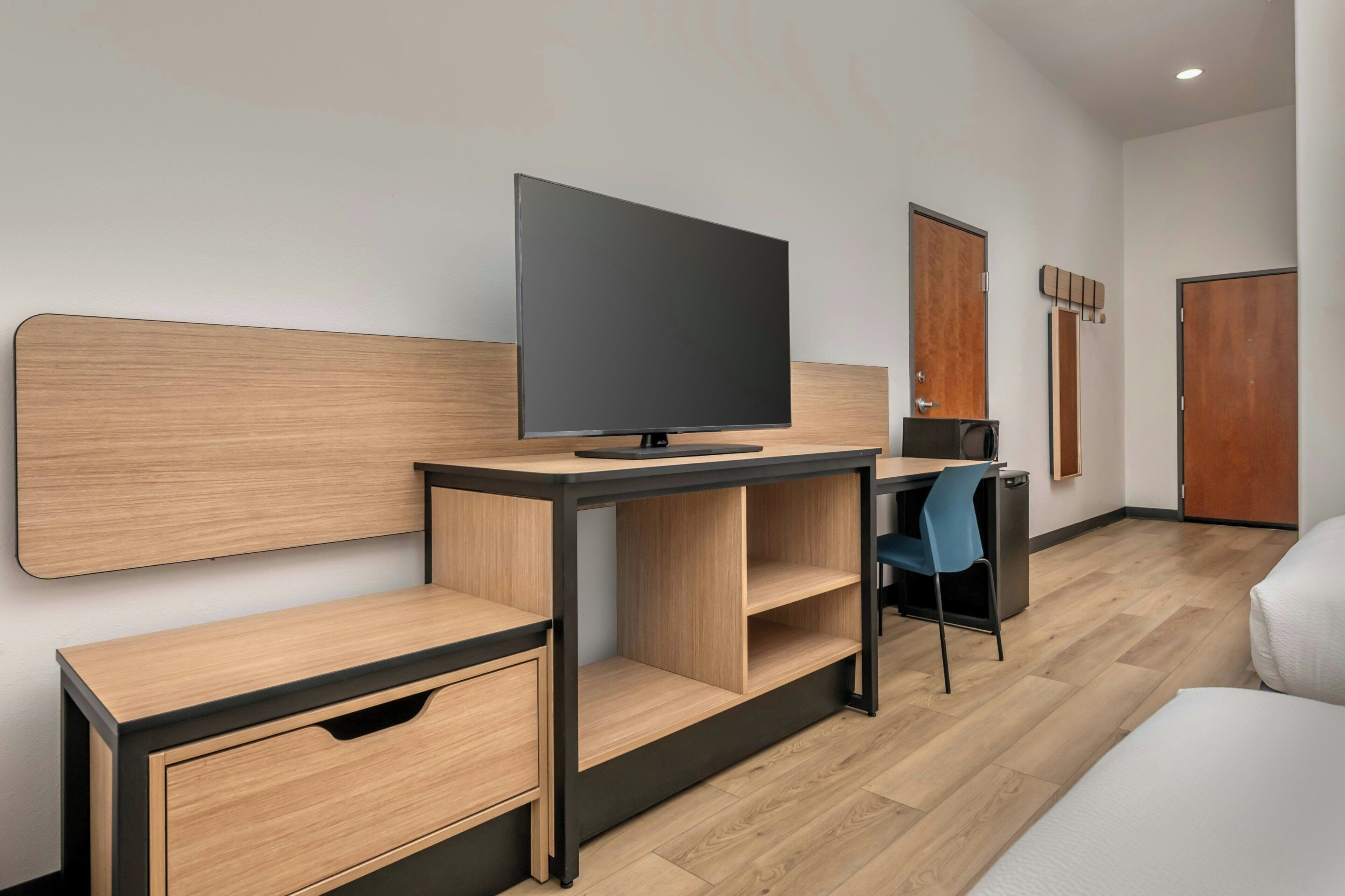 A modern hotel room with a flat-screen TV, a desk with a chair, a wardrobe, and a bed.