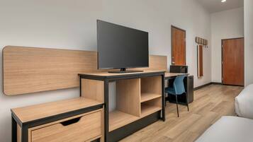 A modern hotel room with a flat-screen TV, a desk with a chair, a wardrobe, and a bed.