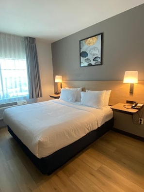 A hotel room with a large bed, two bedside tables with lamps, a wall-mounted artwork, and a window with curtains.