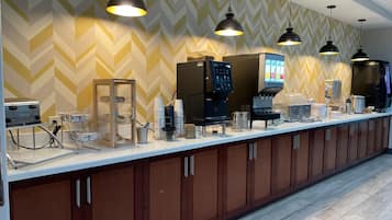 Una barra larga con máquinas de café, una máquina expendedora y una vitrina de vidrio.