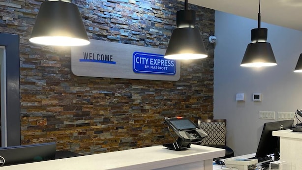 Un comptoir d’accueil avec une pancarte « BIENVENUE » et une autre indiquant « CITY EXPRESS BY MARRIOTT », un mur en pierre et des luminaires suspendus.