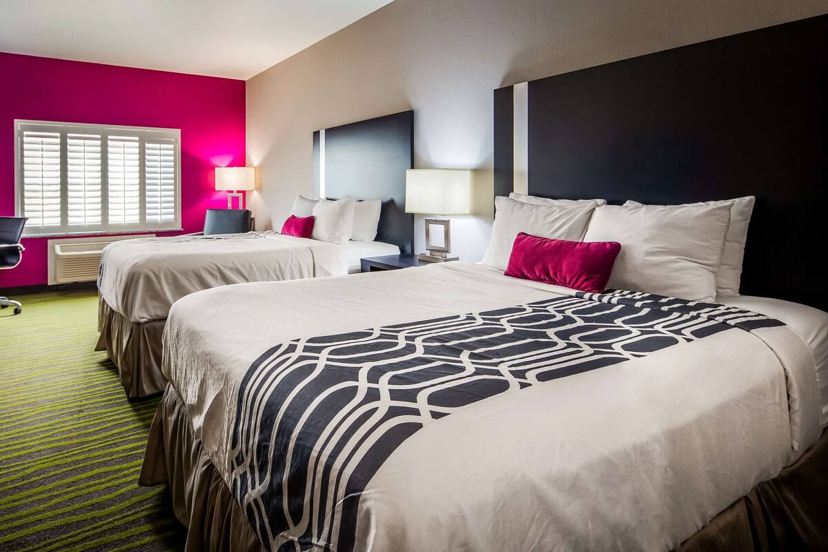 A hotel room with two beds, a desk, a chair, and a TV.