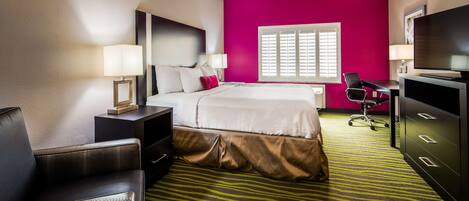 A hotel room with a bed, a desk, a chair, a TV, and a window with blinds.