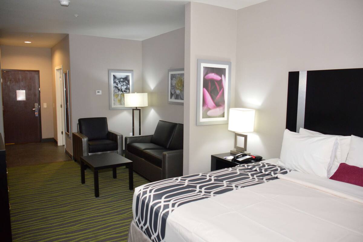 A hotel room with a bed, a desk, a chair, a sofa, and a lamp.