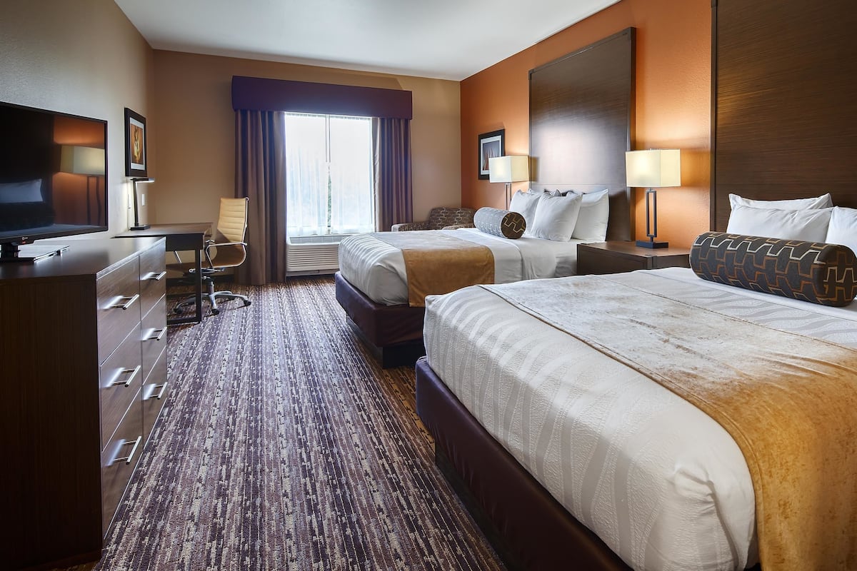 A hotel room with two beds, a desk, a chair, and a TV.