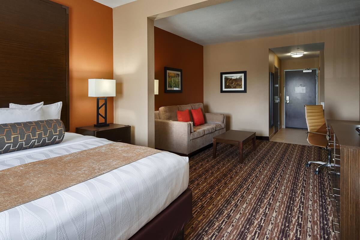 A hotel room with a large bed, a sofa, a desk, and a chair.