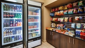 Deux distributeurs de boissons, remplis de diverses boissons, et une étagère avec des en-cas et d’autres produits alimentaires.