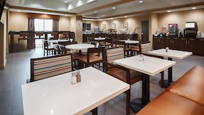 Un espace de restauration d’hôtel comprenant plusieurs tables et chaises, une machine à café et un comptoir de buffet.