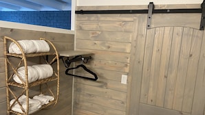Ein Zimmer mit einer Holzwand, einem Korbschrank mit Handtüchern, einem schwarzen Kleiderbügel und einer Schiebetür im Bauernhausstil.