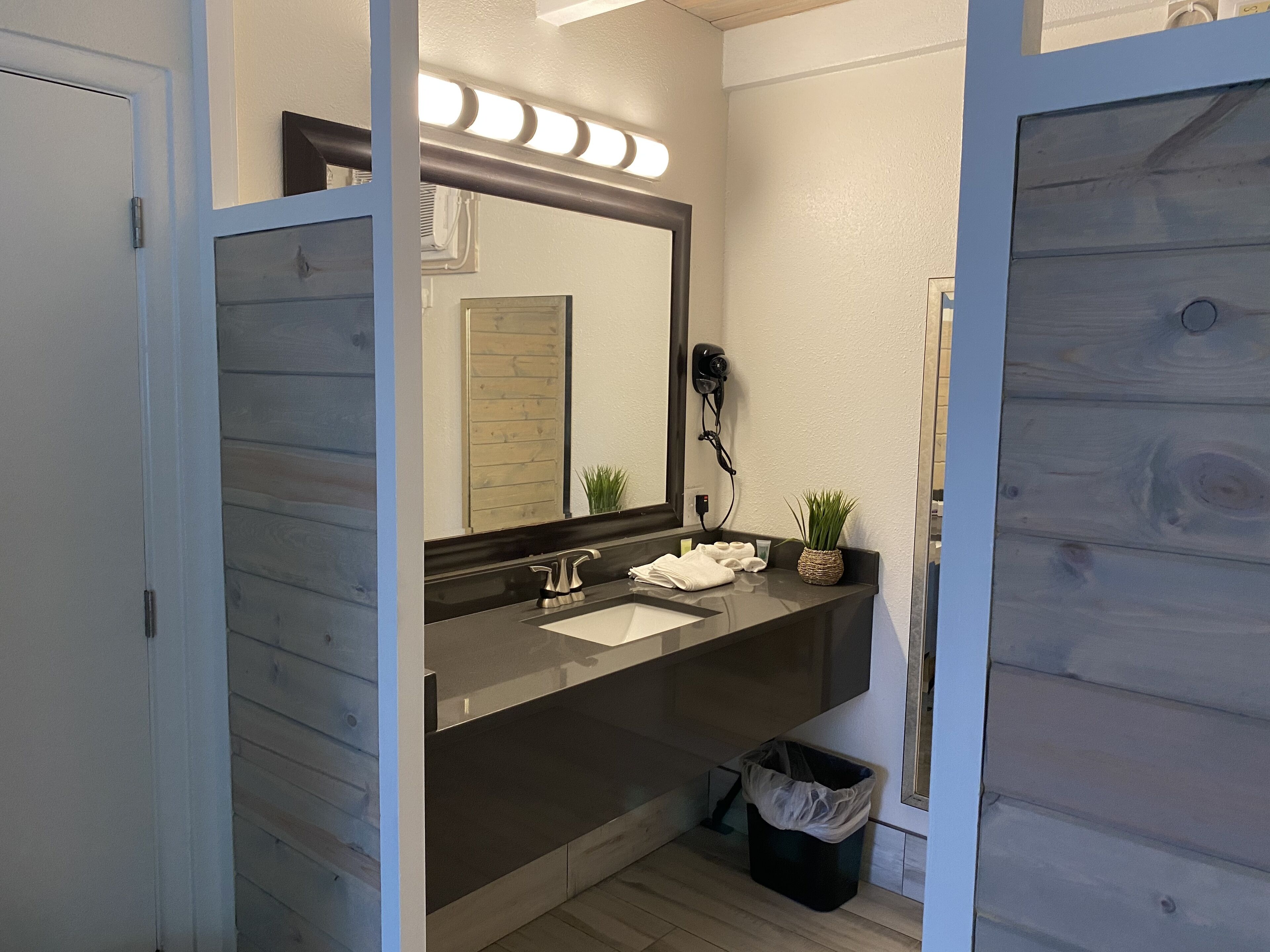 Une salle de bain moderne avec un meuble-lavabo en bois, un grand miroir, un sèche-cheveux et une petite plante.