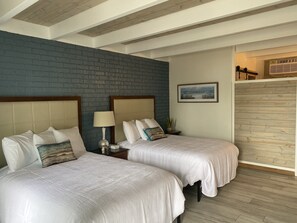 A hotel room with two beds, a brick accent wall, a framed picture, and a wooden ceiling.